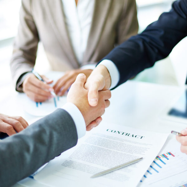 Making agreement Image of business partners handshaking over business objects on workplace